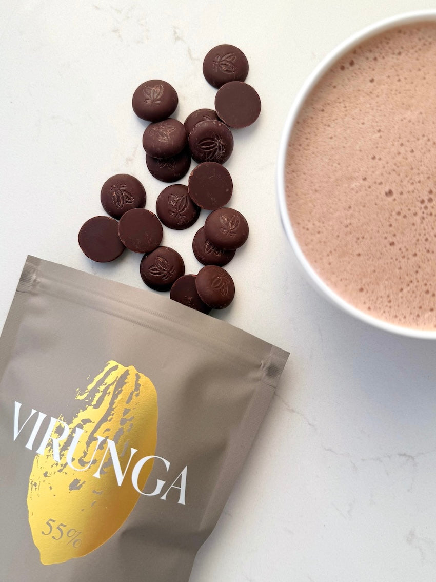 Verpackung der Sorte Virunga, Milch-Schokoladendrops und eine Tasse mit aufgeschäumter Vollmilch-Trinkschokolade.